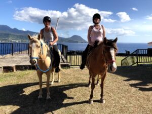 Two guests on horses in front of Dominica ocean shore