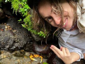 Woman holding up two fingers next to a crab in water