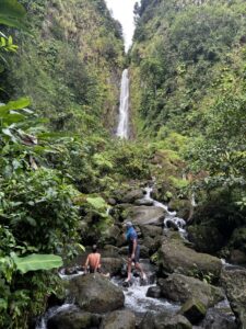 Group of guests sitting on some greey rocks in front of a roaring waterfall in Dominica